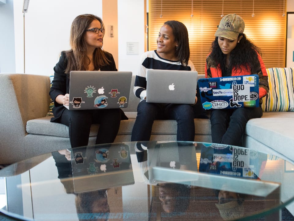 Three colleagues working from laptops on a sofa in an open office